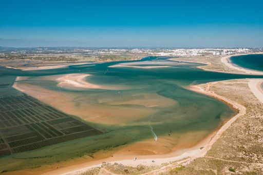 A high angle shot of the fields and the sea under the clear blue sky captured in Algarve, Portugal