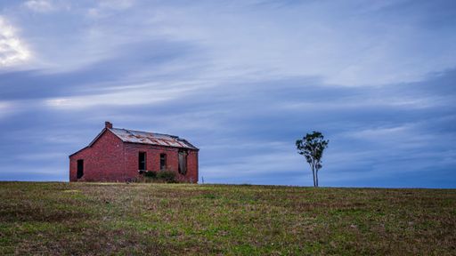 A scenic abandoned old red house in a remote area with a tree next to it
