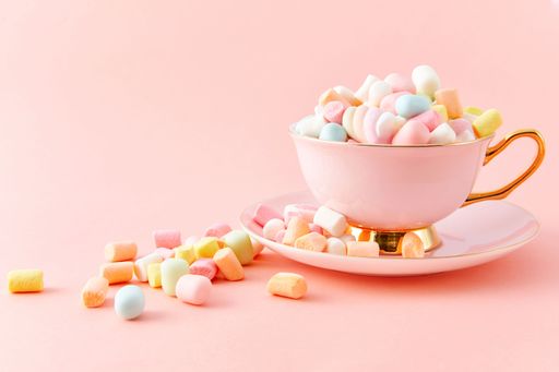 A closeup of a cup filled with colorful marshmallows isolated on a pink background with copy space