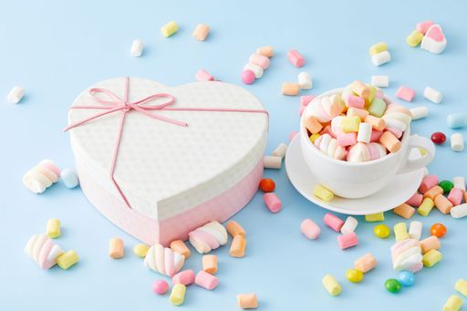 A closeup of a cup filled with marshmallows and a heart-shaped box isolated on a blue background