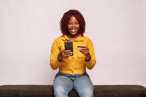 young black lady using her phone and credit card smiling