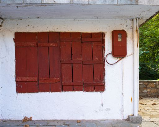 A wooden red window and an electric meter box on an old white wall.