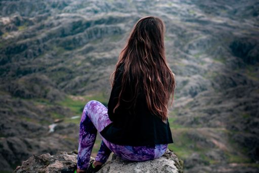The back of a female with long hair sitting on a rock and looking at a beautiful view
