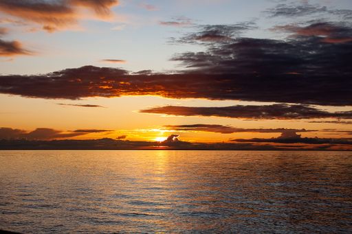 The sun sets behind distant clouds over the bay