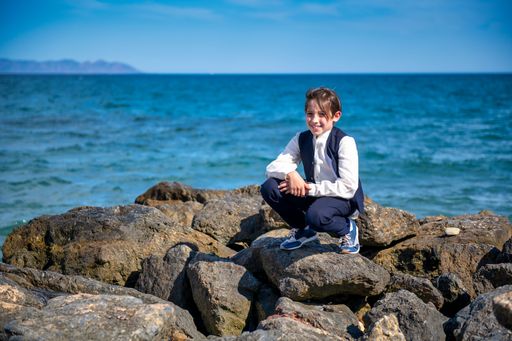 Boy posing in nice clothes on the coast, on rocks with the ocean in the background and a beautiful blue sky with clouds.