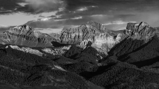 A grayscale shot of rocky landscapes and forested hills against the cloudy gloomy sky