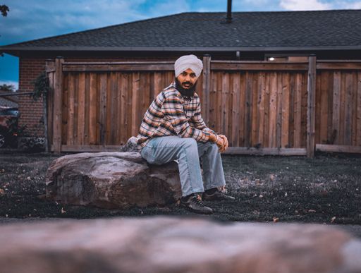 A closeup shot of a South Asian Hindu male sitting on a rock outdoors with wooden fence on the background