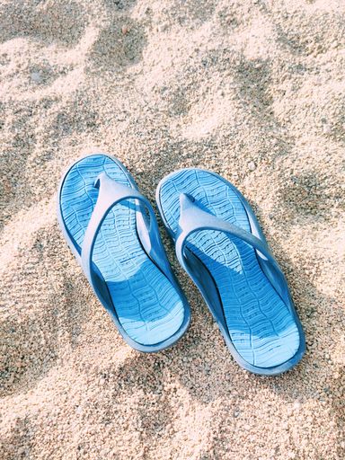 A vertical shot of two blue sandals on the sand on a beach in sunny weather