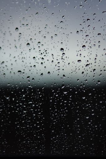 A vertical shot of rain droplets on a glass surface
