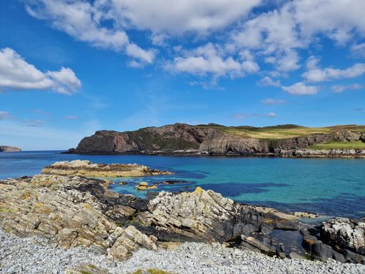 A landscape shot of a rocky coast of a lake surrounded by hills under the cloudy blue sky
