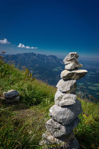 Vertical picture a cairn of small stones in the nature of the Alps.  The stones are in the Alps, where there are high mountains in the background.