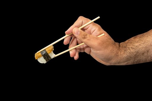 A closeup of a male hand holding a skin nigiri sushi with chopsticks isolated on black background