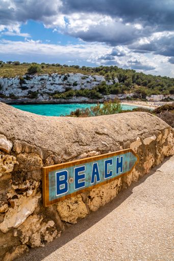 A picturesque stone wall in an idyllic beach setting, adorned with a wooden sign that reads "Beach"