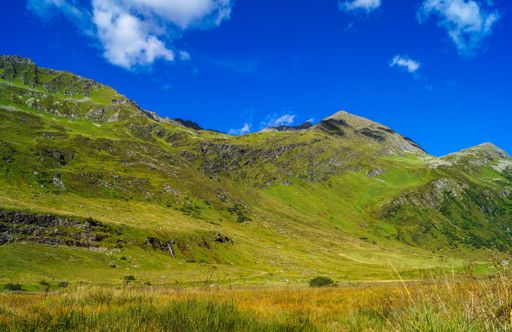 A scenic landscape featuring green mountains and blue sky. Silvretta High Alpine Road, Switzerland.