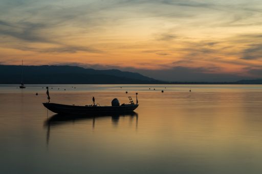 A boat is pictured floating in the middle of a tranquil lake at beautiful sunset.