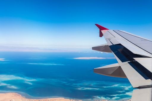 An aerial view of an airplane wing against the background of a blue coral reef and sky. Egypt.