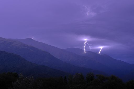 A sudden flash of lightning striking the peak of a mountain under a purple sky covered by a sea of foggy clouds