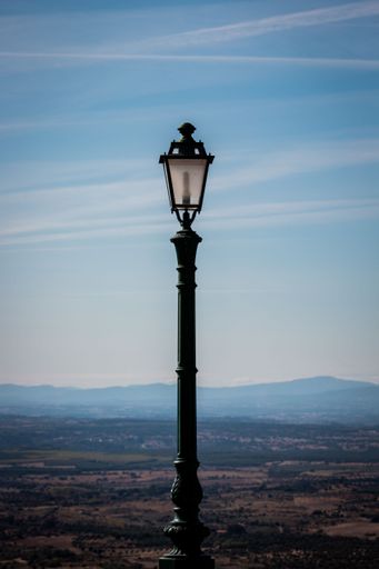 A vertical shot of a lantern against a landscape and a blue sky