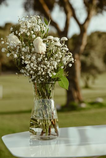 A vertical shot of a glass vase with blooming white flowers on an outdoor table