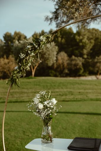 A vertical shot of a glass vase with blooming white flowers on an outdoor table