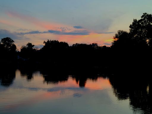A beautiful lake reflects the orange sunset with trees in the background