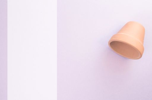 An empty little terracotta flower pot on a light violet surface - top view