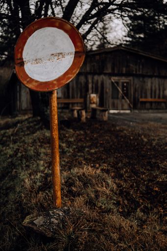 A vertical shot of a round red and white road sign under a tree in front of an old wooden building