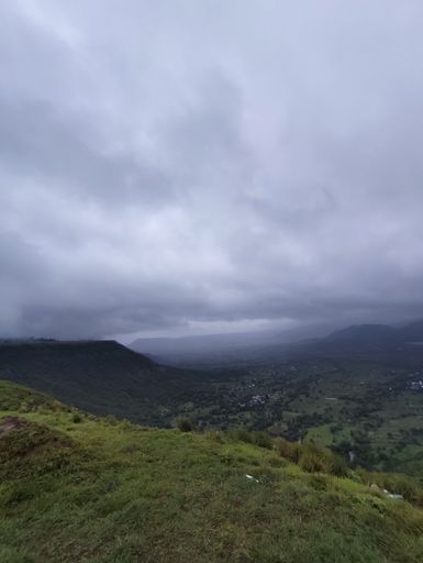 A vertical shot of a cloudy sky over green hills