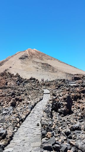 A vertical shot of a rocky pathway leading up to a mountain under a clear blue sky