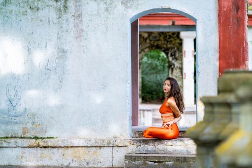 A young brunette woman in orange sportswear practising yoga in a park on a sunny day