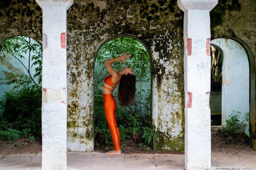 A portrait of a brunette woman in orange sportswear meditating in an old abandoned building