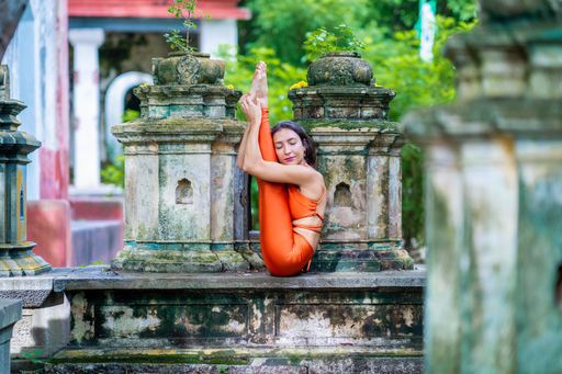 A young brunette woman in orange sportswear practising yoga in a park on a sunny day