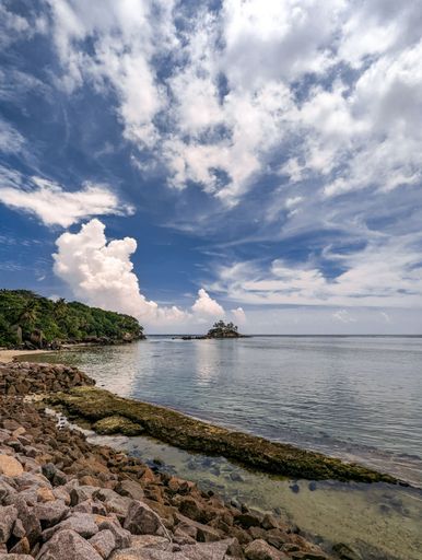 A vertical shot of a rocky beach under a cloudy blue sky