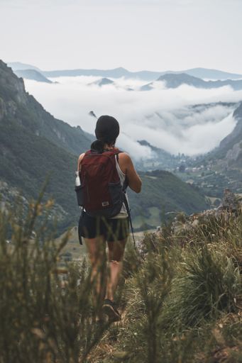 A vertical shot of a female backpacker looking at clouds covering the valley at Somiedo Natural Park in Spain