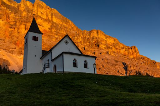 A low-angle shot of a chapel on a hill with the dolomite mountains behind in Badia, Italy