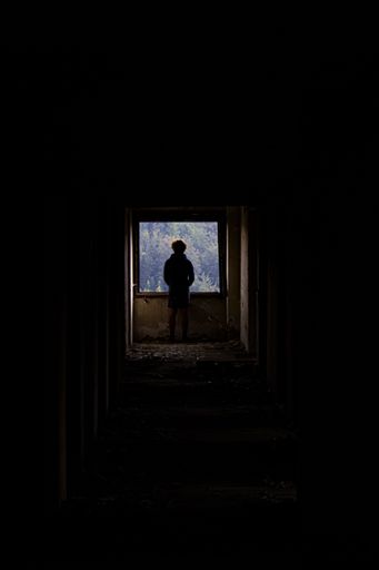 A vertical shot of a silhouetted male standing at the ending of a dark corridor
