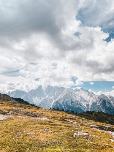 A beautiful vertical shot of a dry hillside with rocky mountains and fluffy clouds in the background