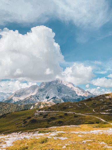 A beautiful vertical shot of a dry hillside with rocky mountains and fluffy clouds in the background