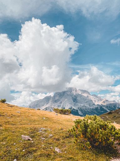 A beautiful vertical shot of a dry hillside with rocky mountains and fluffy clouds in the background