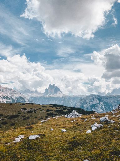 A beautiful vertical shot of a dry hillside with rocky mountains and fluffy clouds in the background