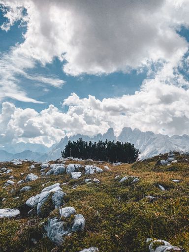 A beautiful vertical shot of a dry hillside with rocky mountains and fluffy clouds in the background