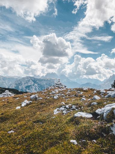 A beautiful vertical shot of a dry hillside with rocky mountains and fluffy clouds in the background
