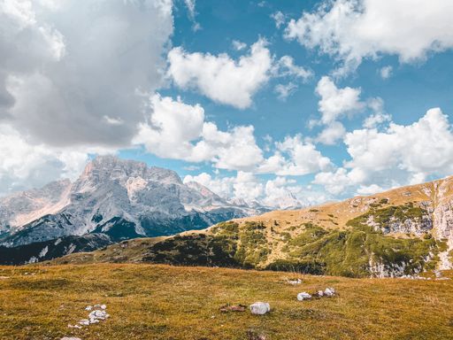 A beautiful view of a dry hillside with rocky mountains and fluffy clouds in the background