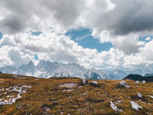 A beautiful view of a dry hillside with rocky mountains and fluffy clouds in the background