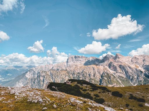 A beautiful view of a dry hillside with rocky mountains and fluffy clouds in the background