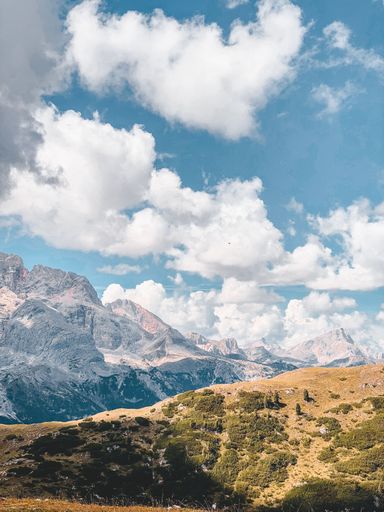A vertical shot of a dry hillside in the Dolomites on a bright sunny day with fluffy clouds in the sky
