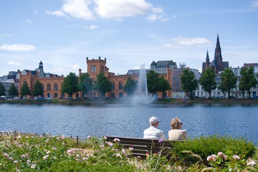 An old couple sits at the lake on a bench and enjoys the sun in Schwerin, Germany