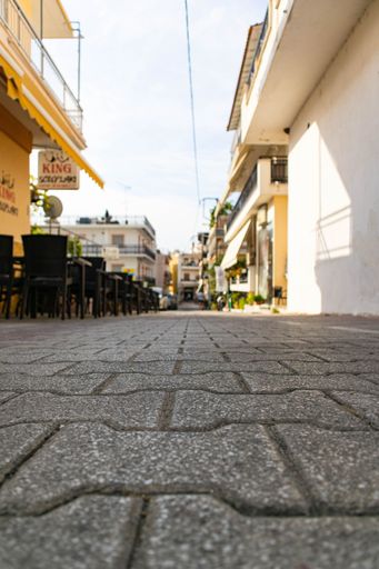 A vertical closeup shot of stone tiles in a street with a cafe building with chairs and tables