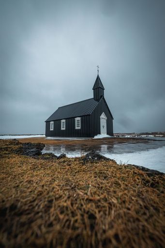 A vertical shot of Budakirkja church and its reflection in the water in front in Budir, Iceland