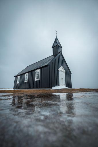 A vertical shot of Budakirkja church and its reflection in the water in front in Budir, Iceland